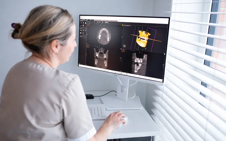 A dentist studying a three-dimensional scan of a jaw on screen while drawing up a treatment plan