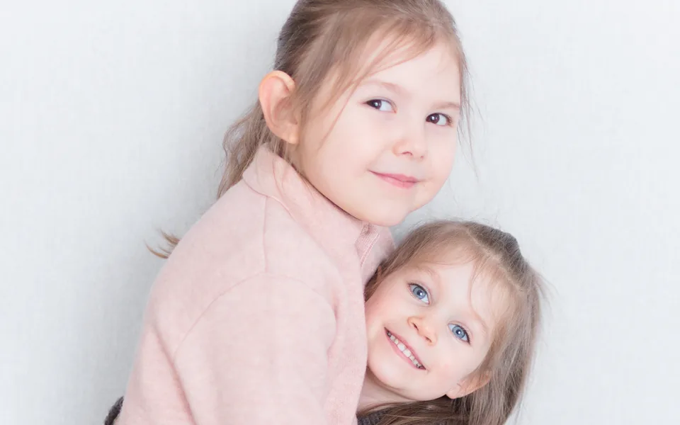Two girls hugging, the younger one holding a toy model of a tooth